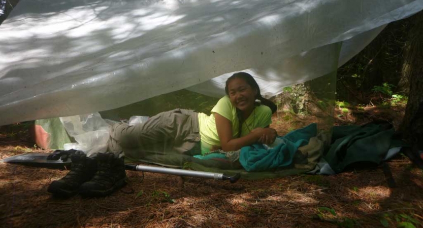 A young person smiles from under a tarp shelter.